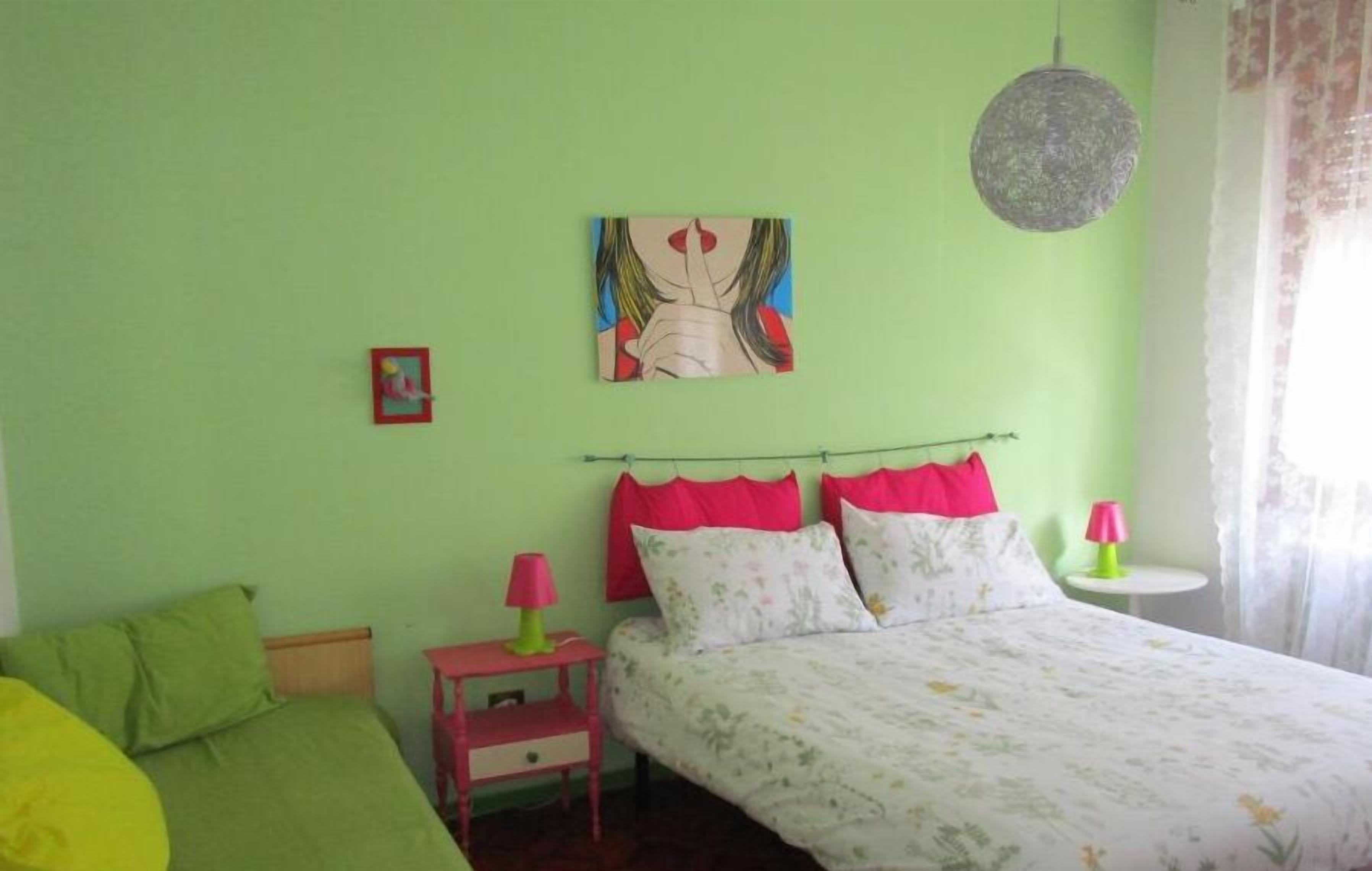 A bedroom with a bed, a nightstand, a lamp, and a painting on the wall.