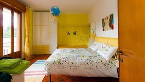 Een kamer met een bed, een gele muur, een raam met gordijnen en een deur.