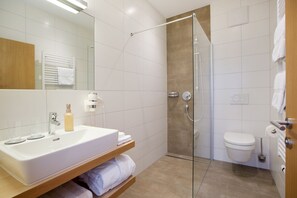 A modern bathroom with a glass-enclosed shower, a white sink with a wooden vanity, and a toilet.