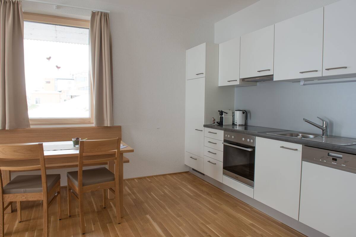 A modern kitchen with white cabinets, a wooden dining table, and chairs.