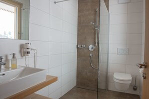 A modern bathroom with a glass-enclosed shower, a white sink with a wooden countertop, and a toilet. - Appartements Berg 170 (Damüls)