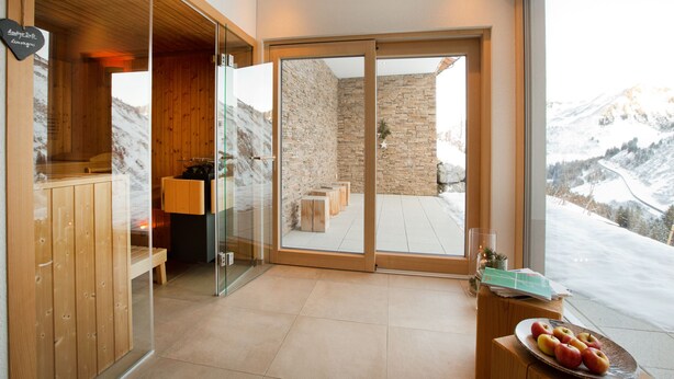A modern interior with a wooden reception desk, a glass partition, and a view of a snowy mountain landscape. - Appartements Berg 170 (Damüls)