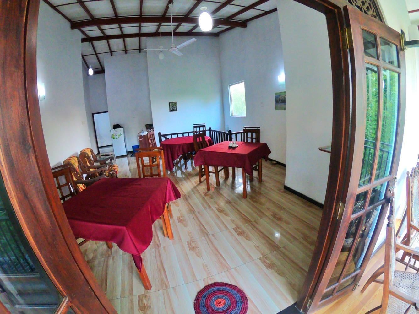 Un'area pranzo con tavoli e sedie di legno, una tovaglia rossa e una ventola a soffitto.