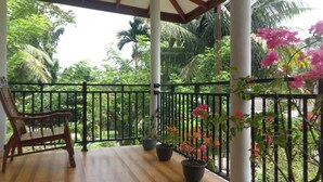 Une terrasse en bois avec une rambarde noire, une chaise en bois et des plantes en pot ornées de fleurs roses.