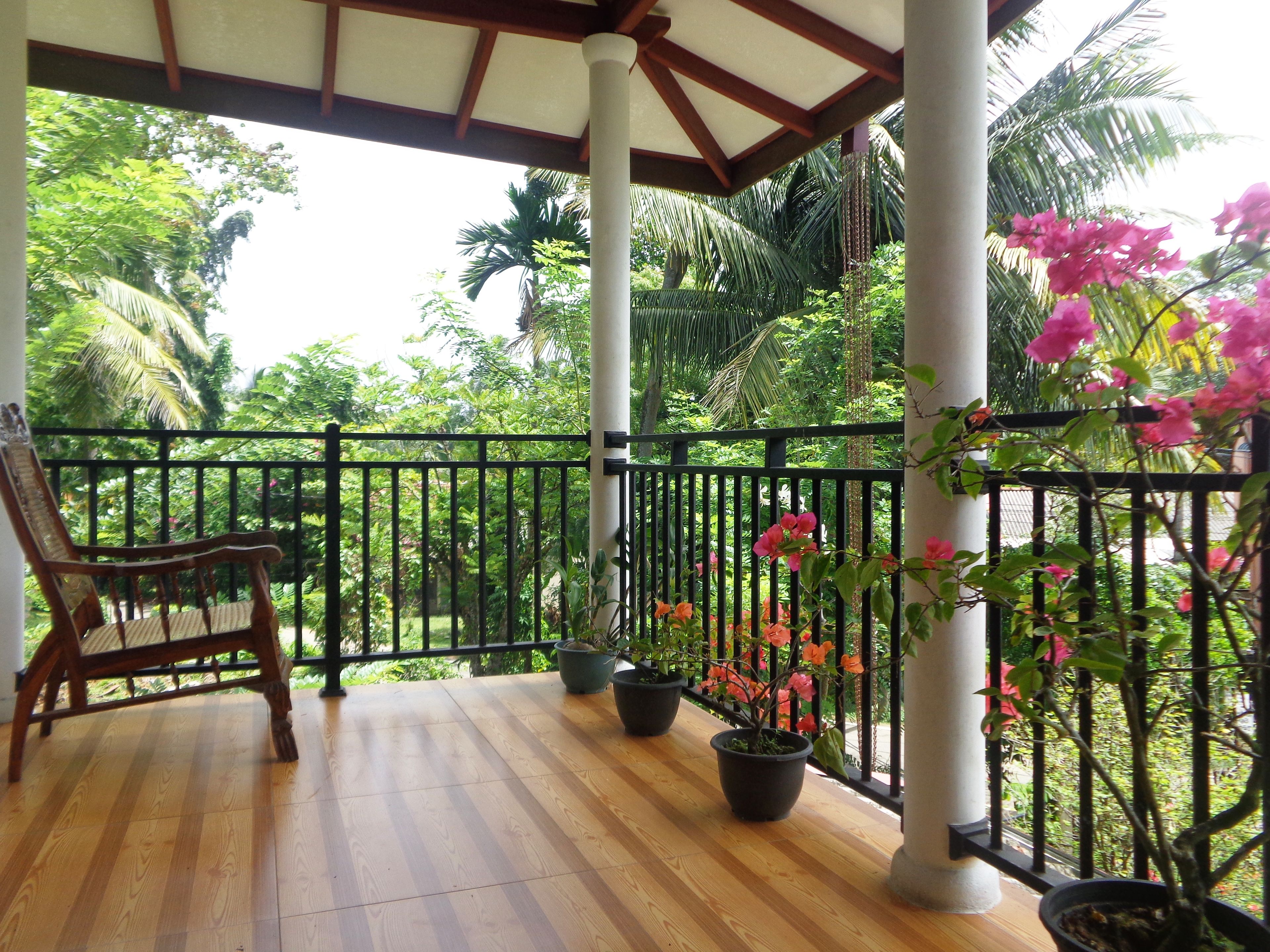 A wooden deck with a black railing, potted plants, and a wooden chair.