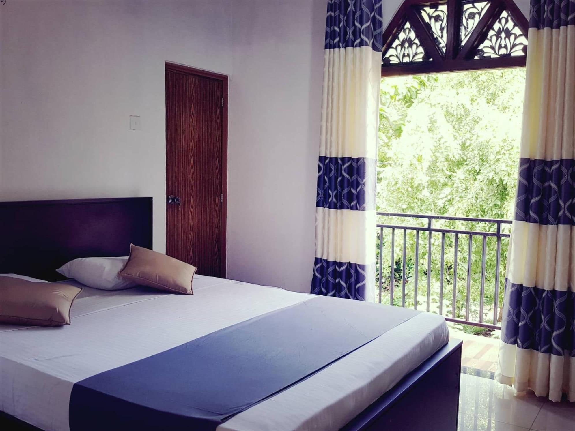 A bedroom with a bed, pillows, a wooden door, and a balcony with patterned curtains.