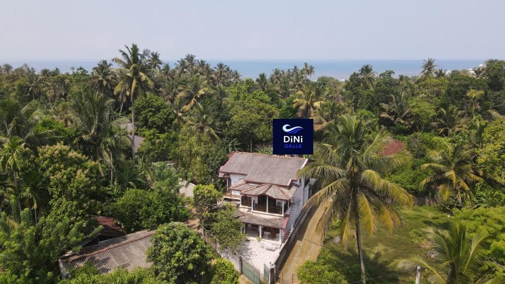 A coastal property with a prominent sign for DiNi Galle, surrounded by dense tropical vegetation and a view of the sea.