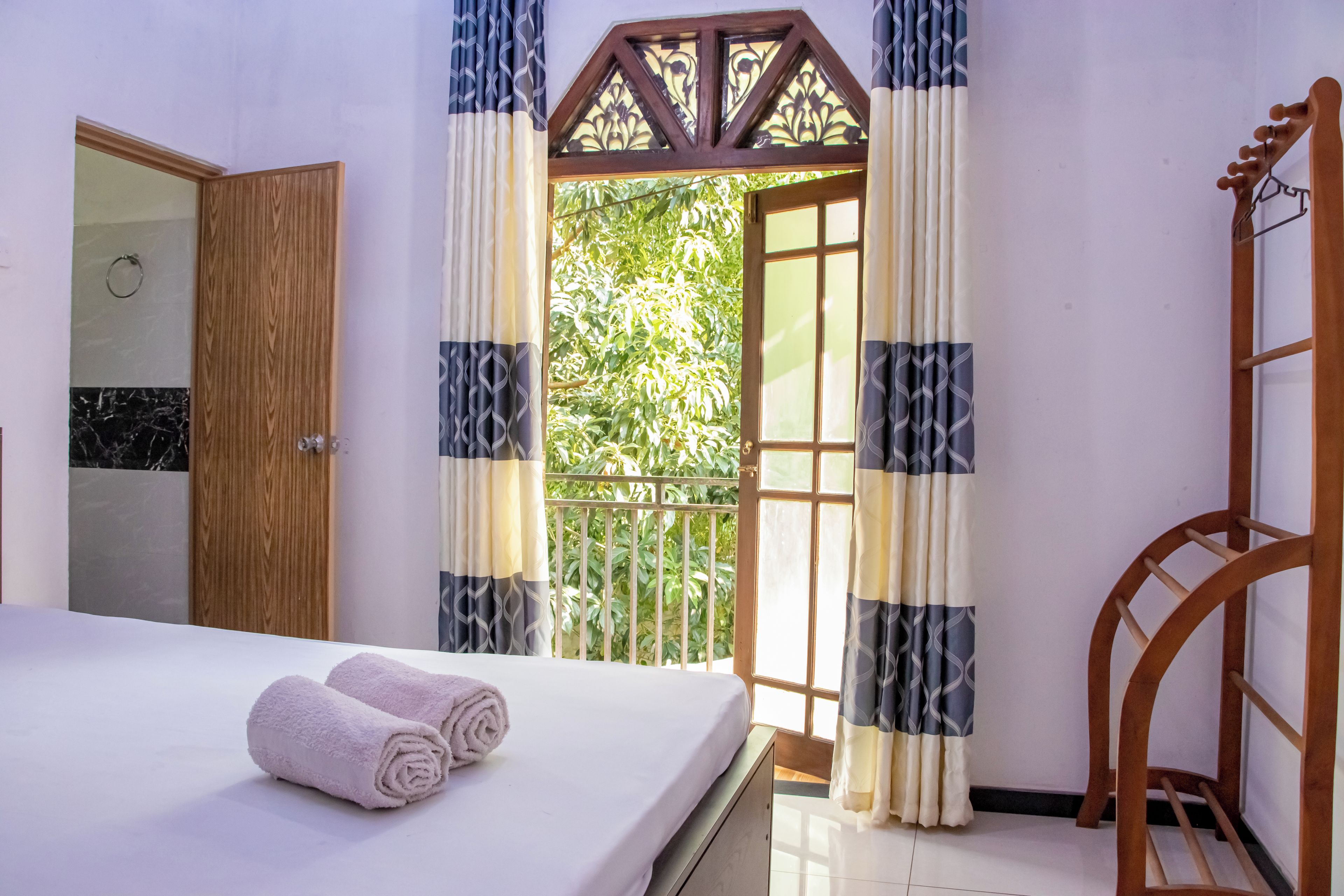 A hotel room with a bed, a wooden door, and a balcony with curtains.