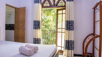 A hotel room with a bed, a wooden door, and a balcony with curtains.