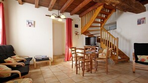 Un saló acollidor amb escala de fusta, zona de dinar amb cadires, sofà i televisió.
