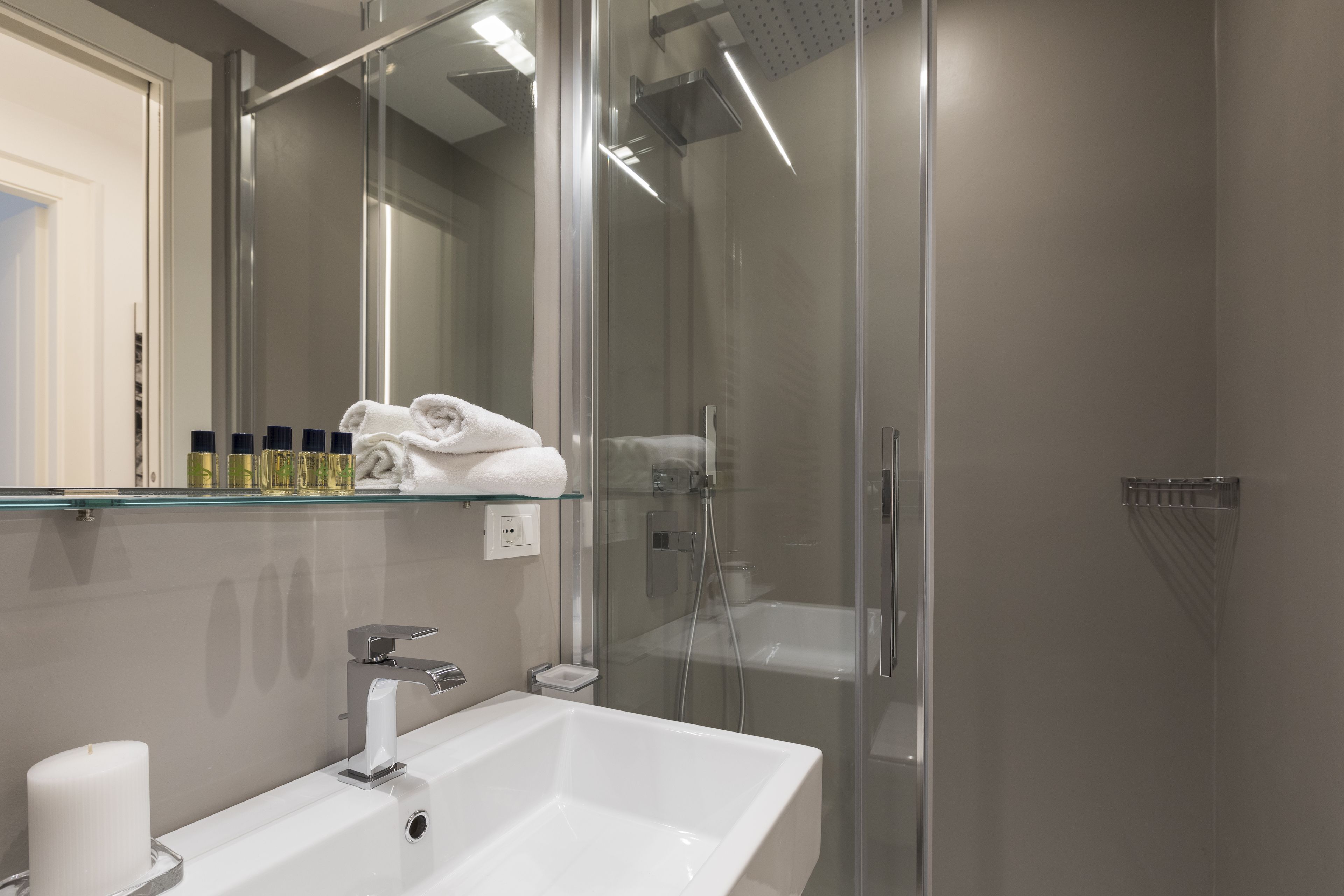 A modern bathroom with a glass-enclosed shower, a white sink, and a glass shelf with toiletries.