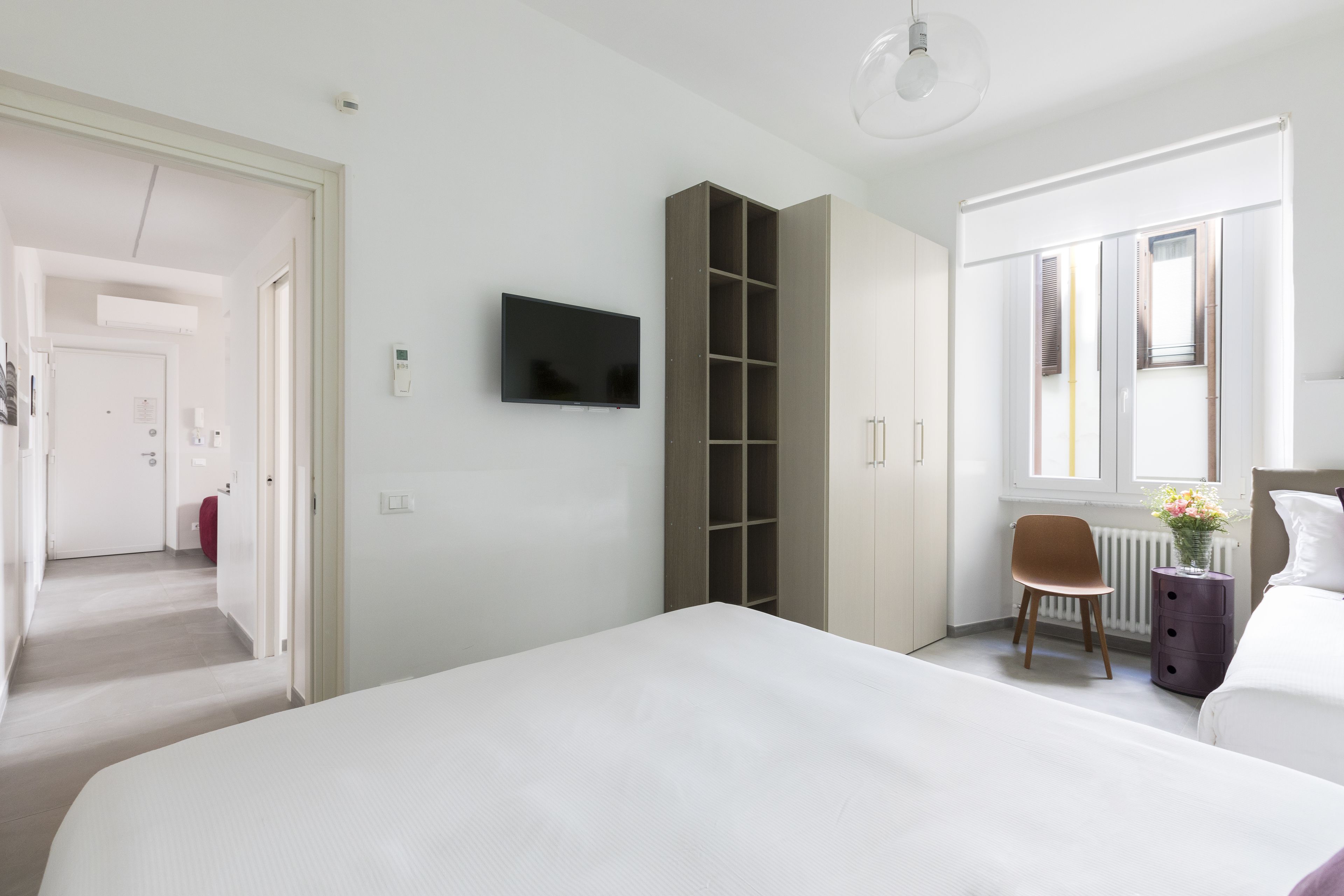 Une chambre d’hôtel moderne dotée d’un grand lit, d’un téléviseur fixé au mur, d’une armoire, d’un petit bureau avec une chaise et d’une fenêtre donnant sur l’extérieur.