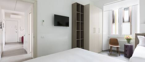 Moderni hotellihuone, jossa on suuri sänky, seinälle asennettu televisio, vaatekaappi, pieni työpöytä tuolilla sekä ikkuna, josta on näkymä ulos.