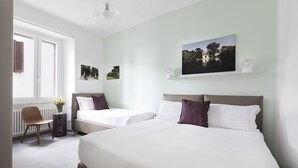 Et hotelværelse med to senge, en stol, et lille bord og en radiator.