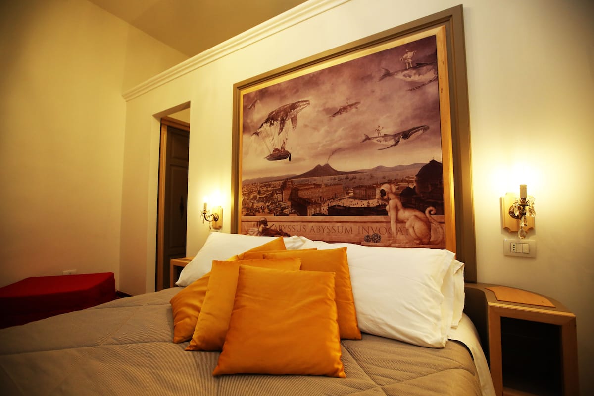 A hotel room with a large bed, a red bench, and a wall painting.