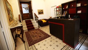 A hotel lobby with a staircase, a reception desk, a bookshelf, and a patterned rug. - La Bella Napoli B&B (Naples)