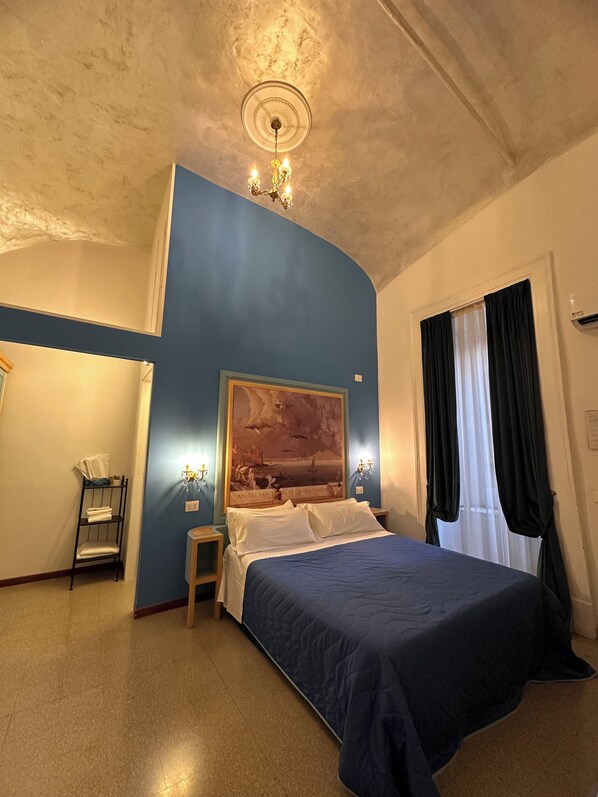 Une chambre à coucher avec un lit, un tableau au mur, un lustre et une fenêtre avec des rideaux.