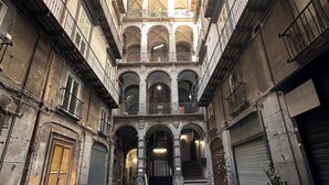 A narrow courtyard with stone flooring, multiple balconies, and a central staircase leading to an upper level. - La Bella Napoli B&B (Naples)