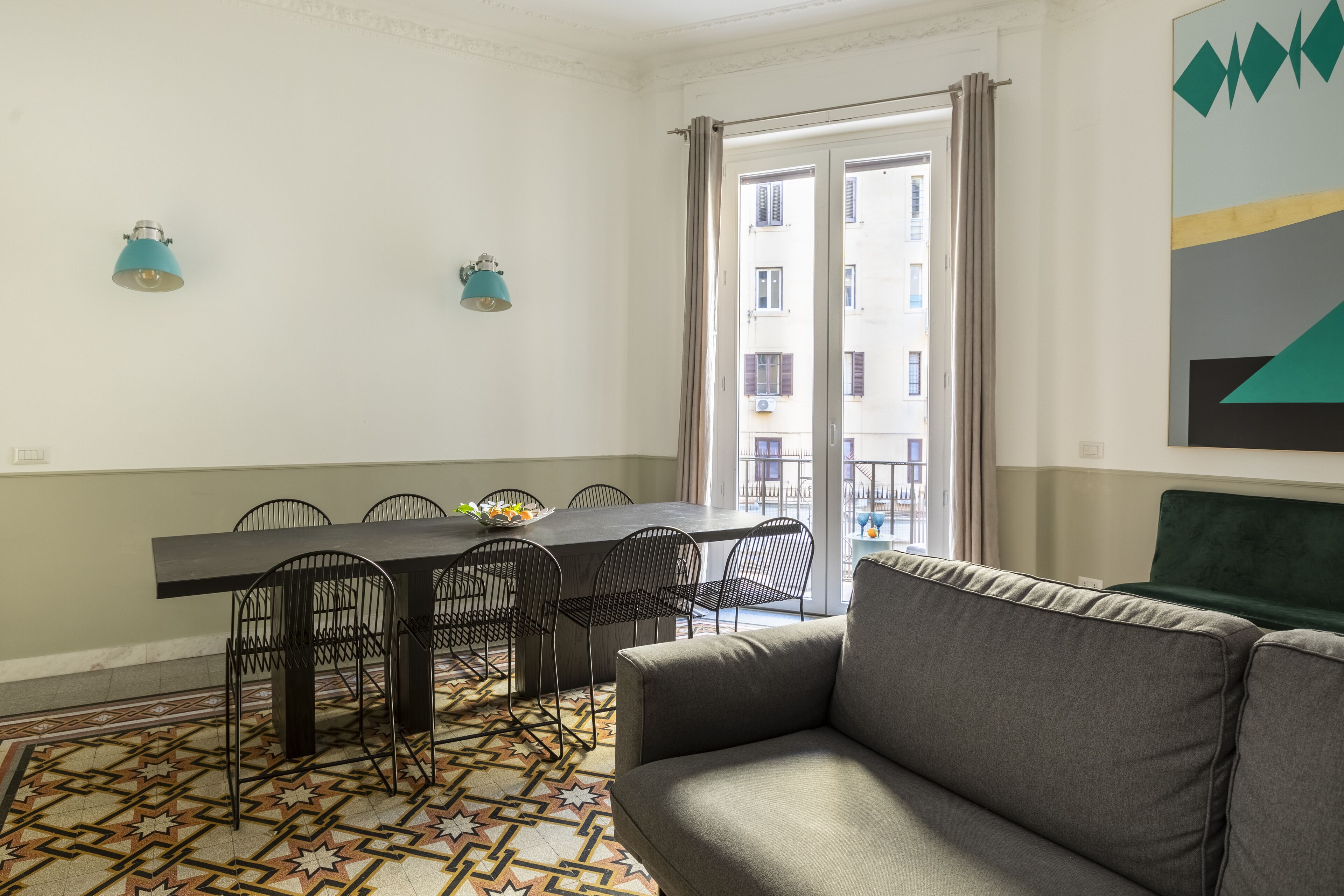 A modern living room with a grey sofa, a dining table with chairs, and a patterned floor.