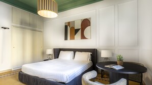 A hotel room with a large bed, a round table with a chair, a wall-mounted artwork, and a ceiling light fixture. - ROMAC - Mazzini (Rome)