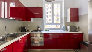 A kitchen with red cabinets, a stainless steel sink, a stove, and a window with a view of buildings. - ROMAC - Mazzini (Rome)