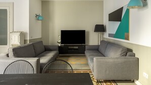 A modern living room with a flat-screen TV, grey sofas, a dining table, and a patterned rug. - ROMAC - Mazzini (Rome)
