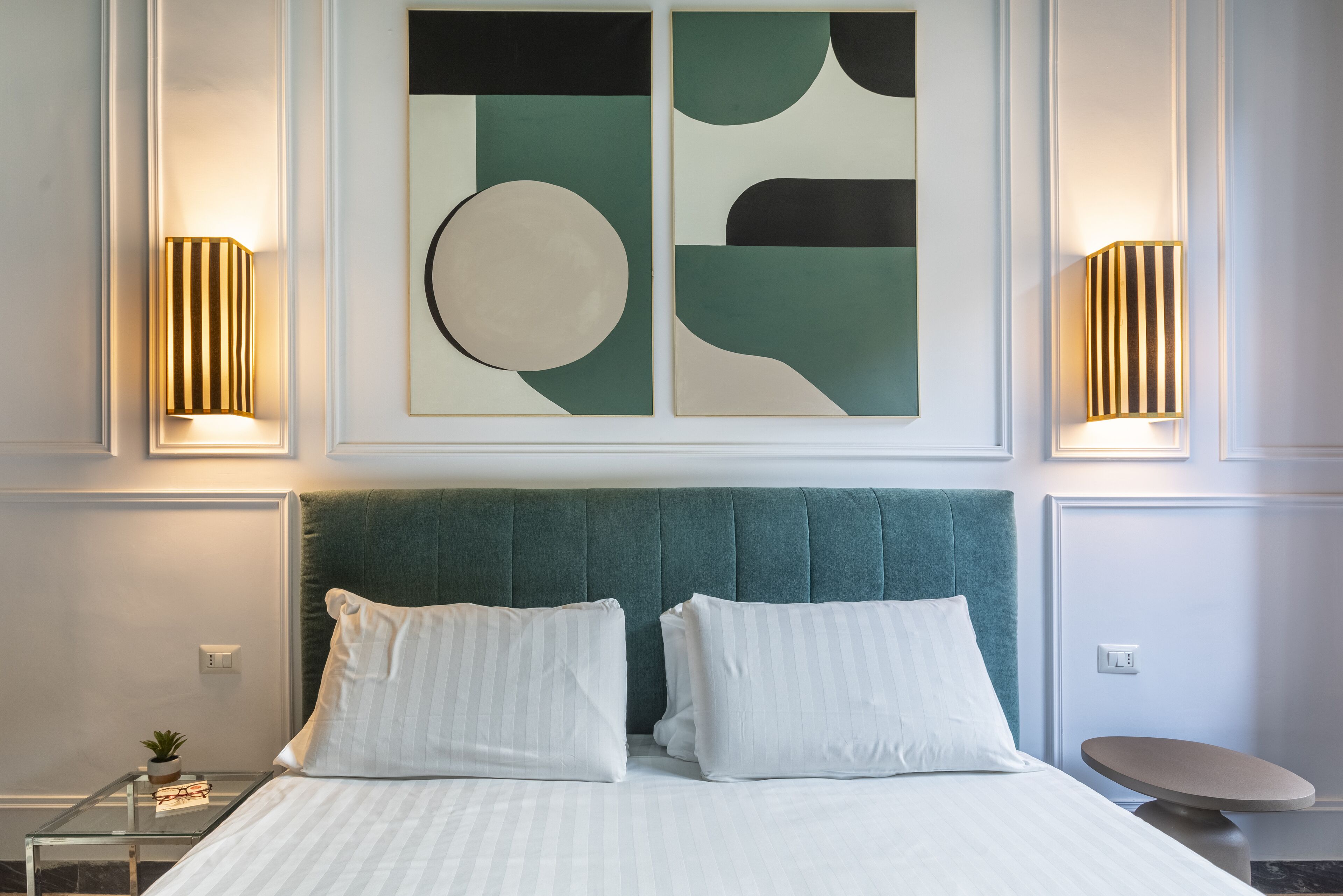 Een hotelkamer met een groot bed, twee bedlampjes, een ronde tafel en een abstract schilderij aan de muur.