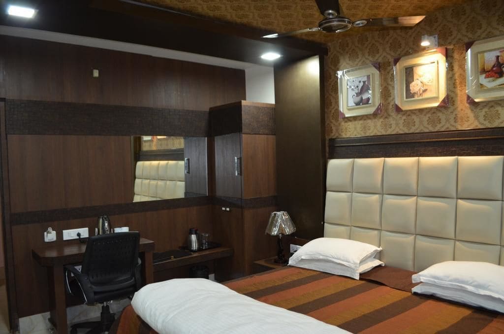 A hotel room with a bed, a desk, a chair, a wardrobe, and a headboard with a mirror.