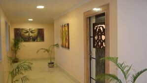 Un pasillo con dos grandes cuadros abstractos, una puerta de madera decorativa y plantas en macetas.