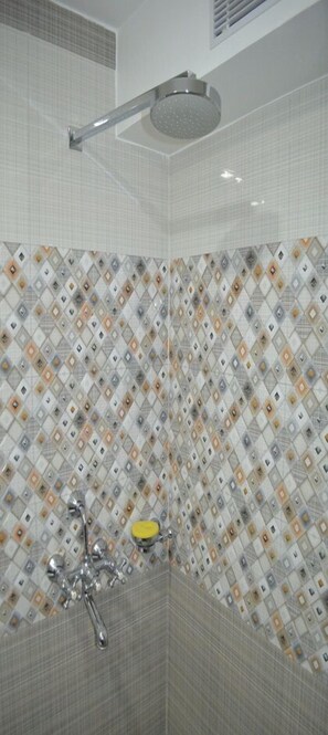 A shower area with a handheld showerhead, a wall-mounted control panel, and a yellow soap dish.