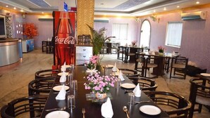 Un comedor con mesas dispuestas para el servicio, un anuncio de Coca-Cola y un centro de mesa con planta decorativa.
