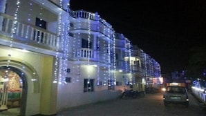 Un edificio con varios balcones decorados con luces colgantes, una entrada empedrada y una motocicleta estacionada.