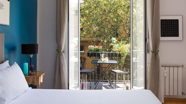 Et hotelværelse med seng, et lille bord med lampe, samt udsigt til en balkon med bord og stole.