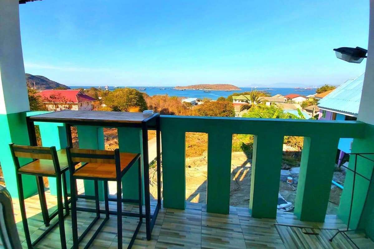 Un balcón con mesa y sillas, con vistas a una zona costera con casas y al mar.