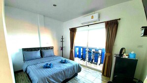 Habitación de hotel con cama, escritorio, silla, ventana con cortinas y balcón con sillas.