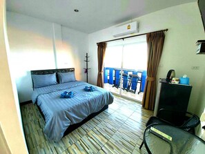 A hotel room with a bed, a desk, a chair, a window with curtains, and a balcony with chairs.