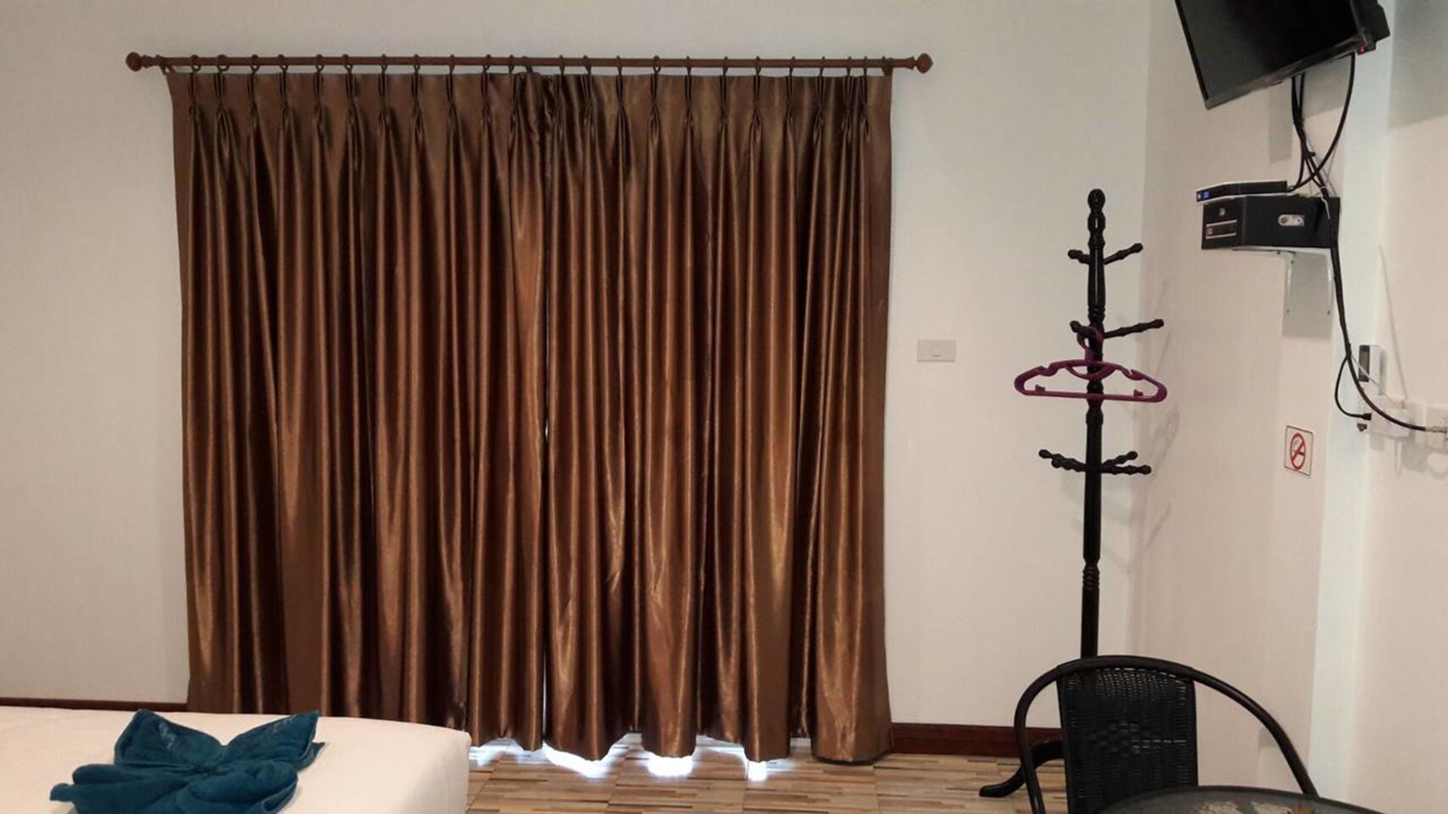 A room with a brown curtain, a bed with a blue pillow, a black chair, and a coat rack with hangers.