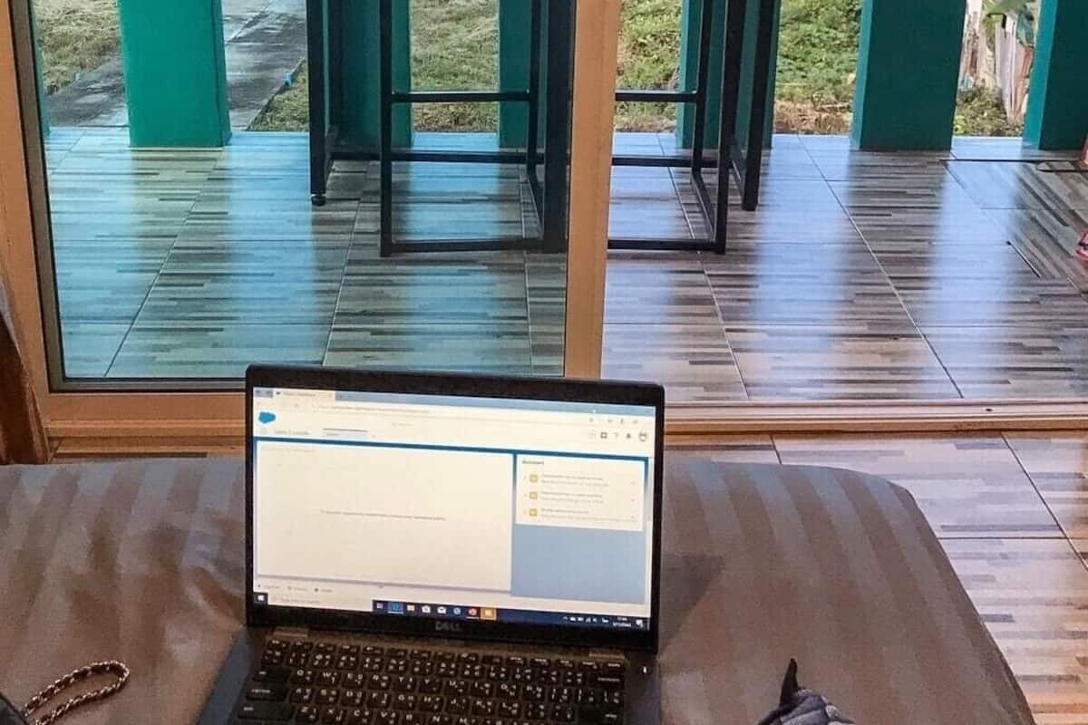 Un ordenador portátil sobre una mesa, con vistas al mar y una terraza con sillas y mesas.