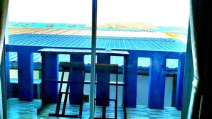 Una habitación con vista al océano a través de amplios ventanales, una terraza de madera y una barandilla azul.
