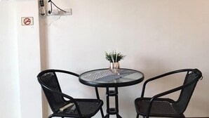 Una habitación pequeña con una mesa redonda y dos sillas, un televisor de pantalla plana montado en la pared y un cartel de prohibido fumar.