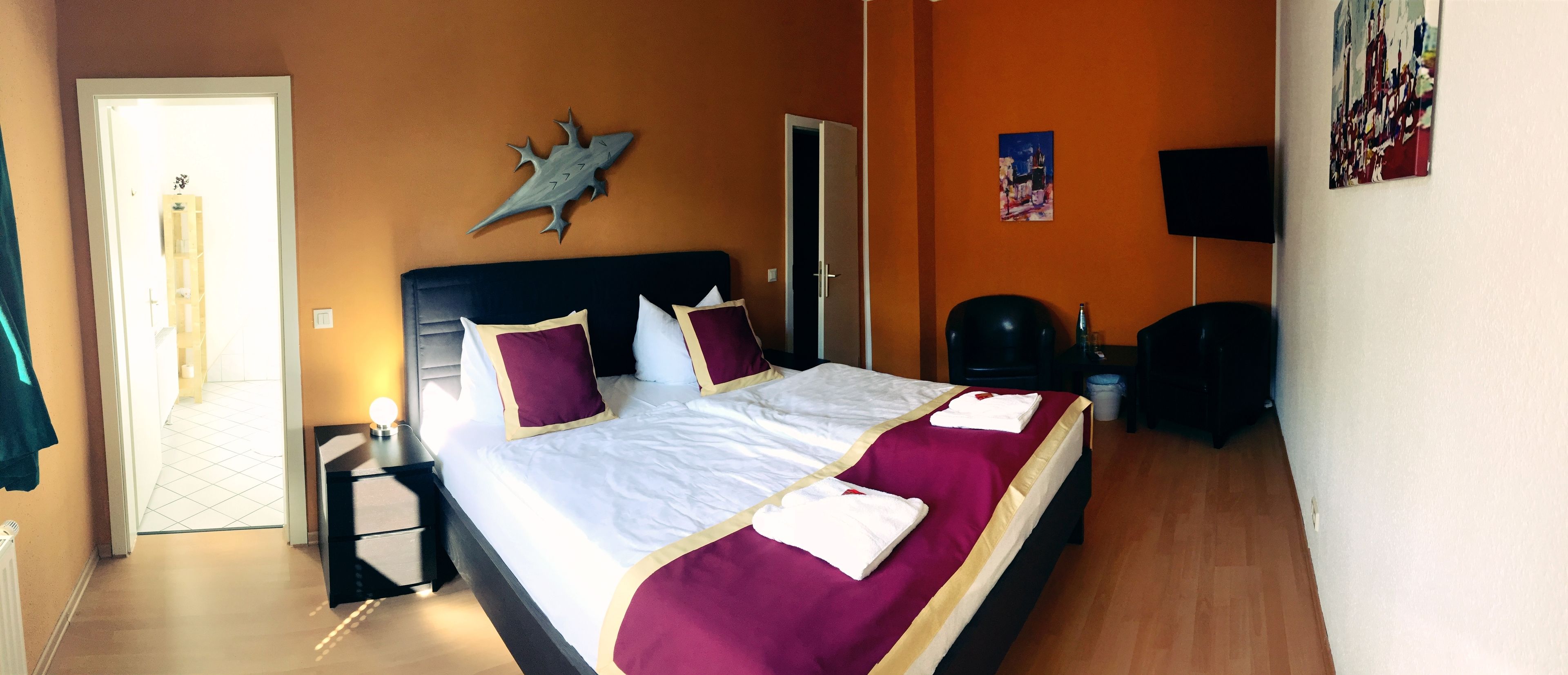 A hotel room with a bed, a nightstand, a wardrobe, a door, and a wall-mounted TV.