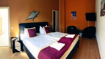 A hotel room with a bed, a nightstand, a wardrobe, a door, and a wall-mounted TV.