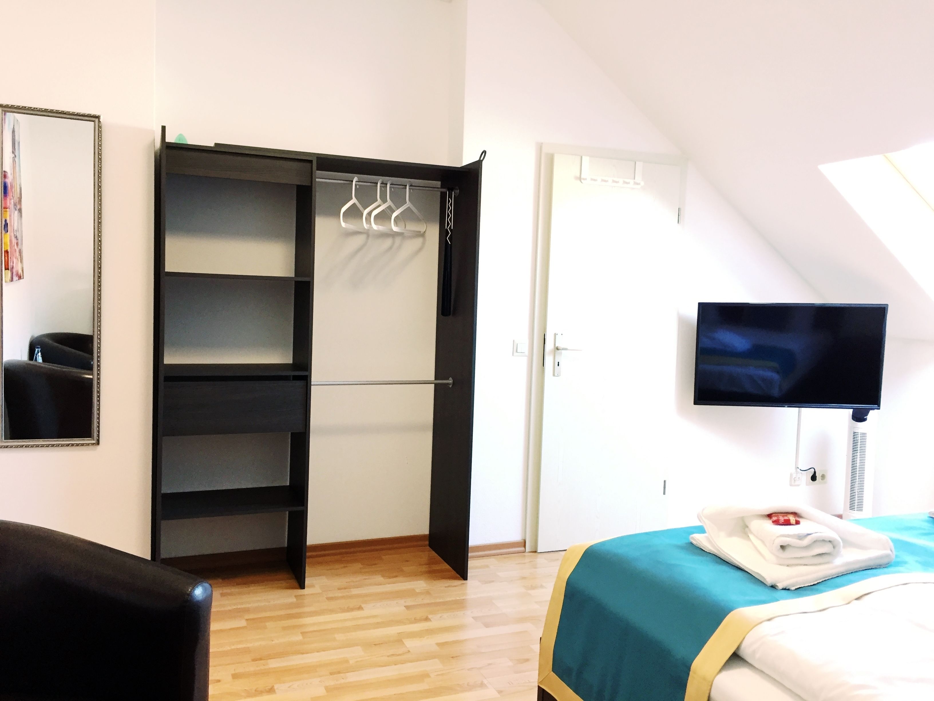 A hotel room with a wardrobe, a bed, a television, and a mirror.