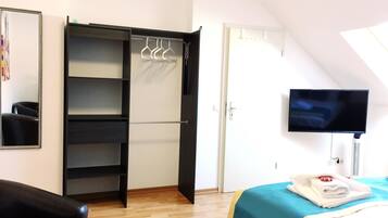A hotel room with a wardrobe, a bed, a television, and a mirror.