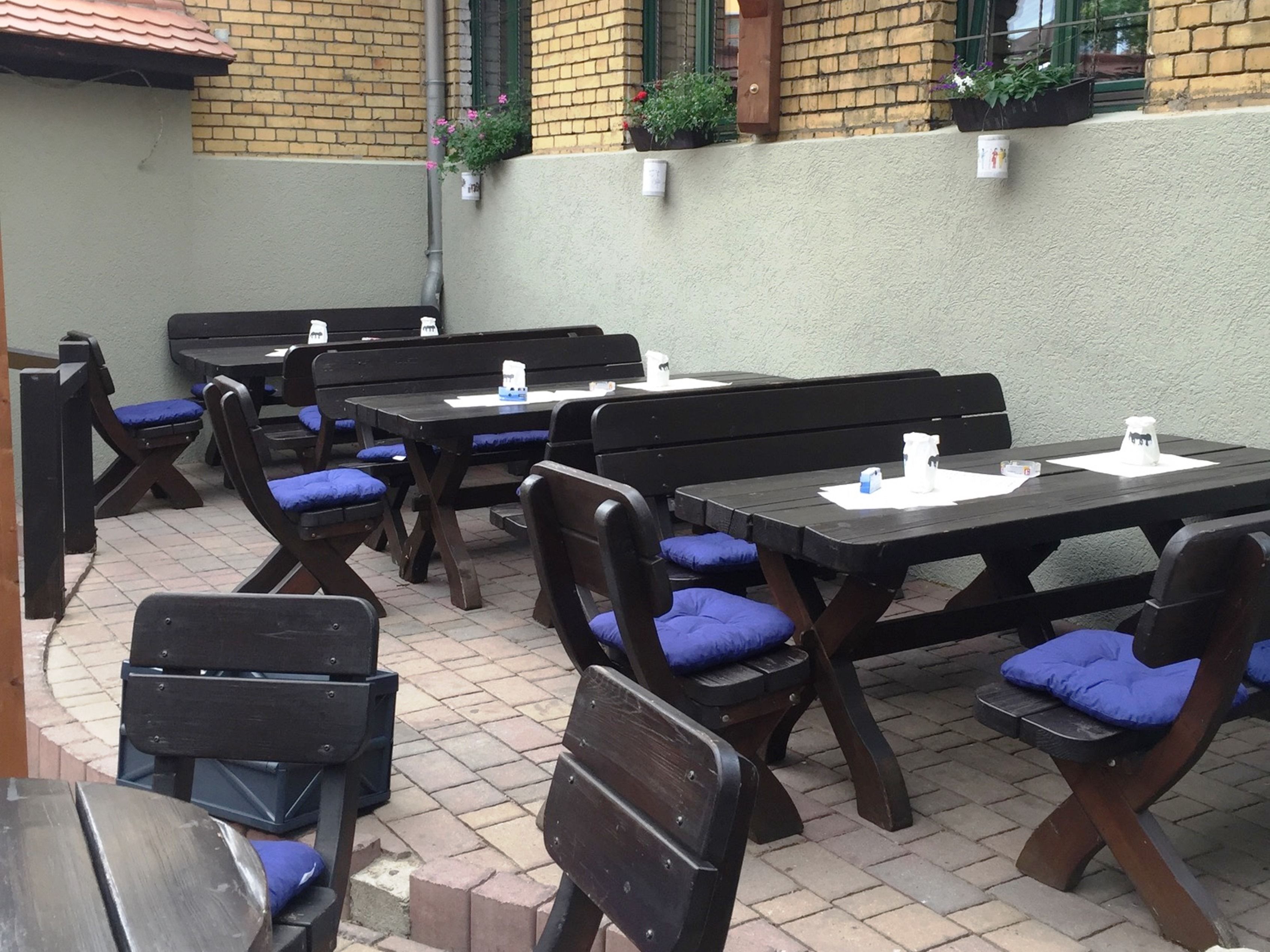 Une terrasse extérieure avec des tables et des bancs en bois, dont certains sont agrémentés de coussins bleus.