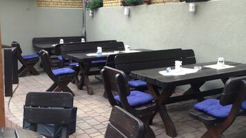 Une terrasse extérieure avec des tables et des bancs en bois, dont certains sont agrémentés de coussins bleus.
