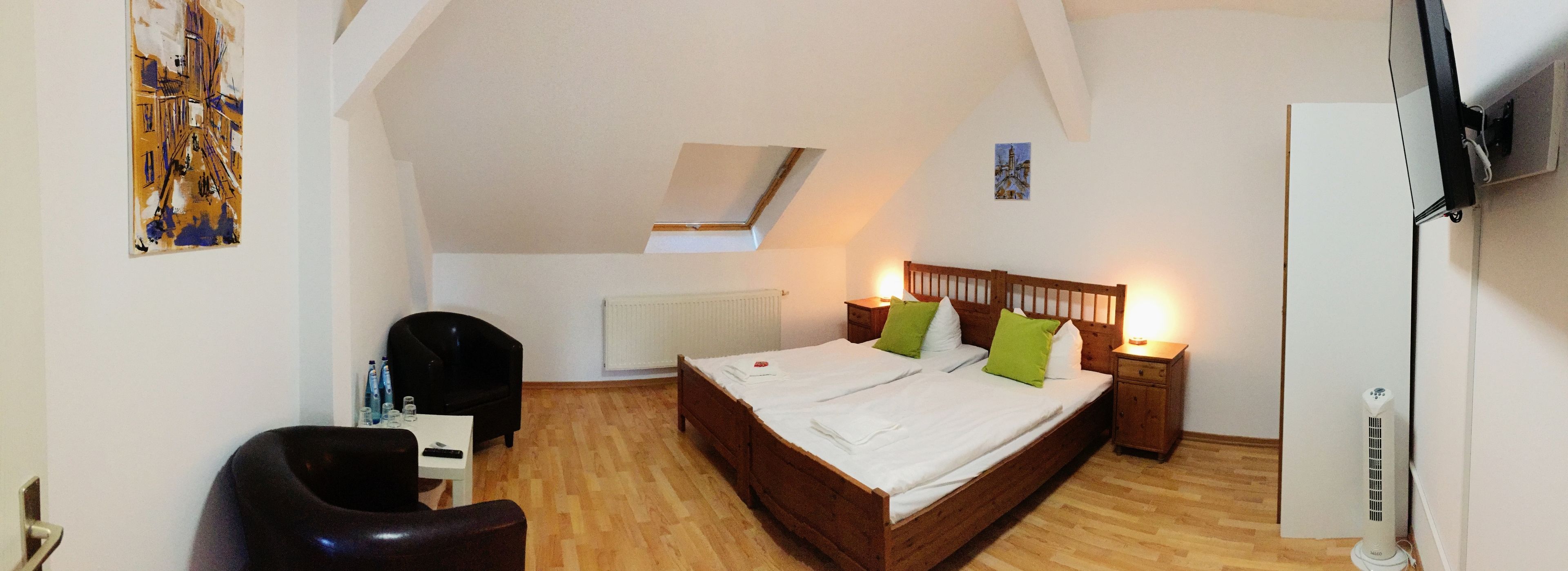 A bedroom with a wooden bed, a desk, a chair, a radiator, a ceiling fan, and a painting on the wall.