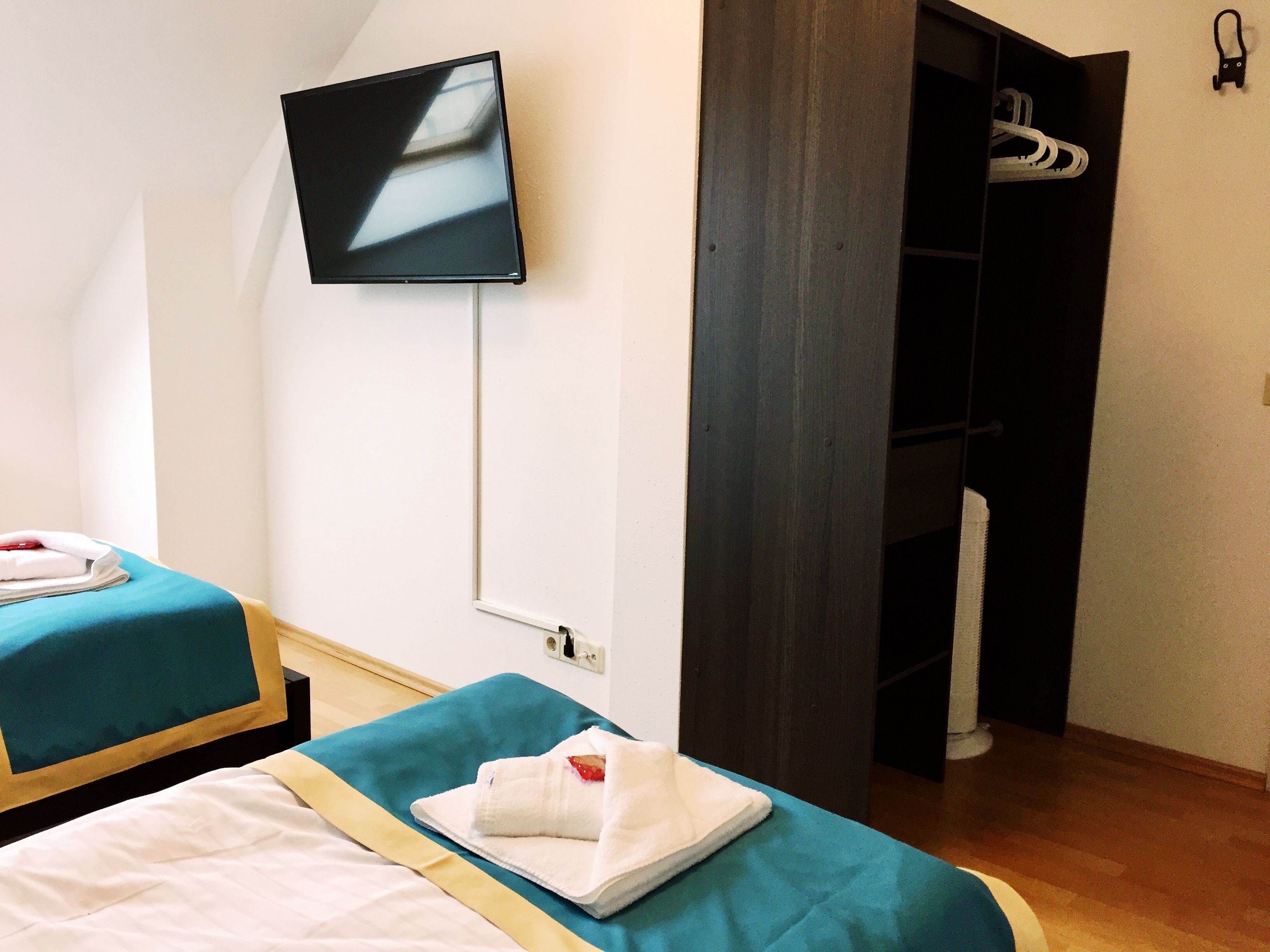 Een hotelkamer met twee bedden, een aan de muur bevestigde televisie en een kledingkast.