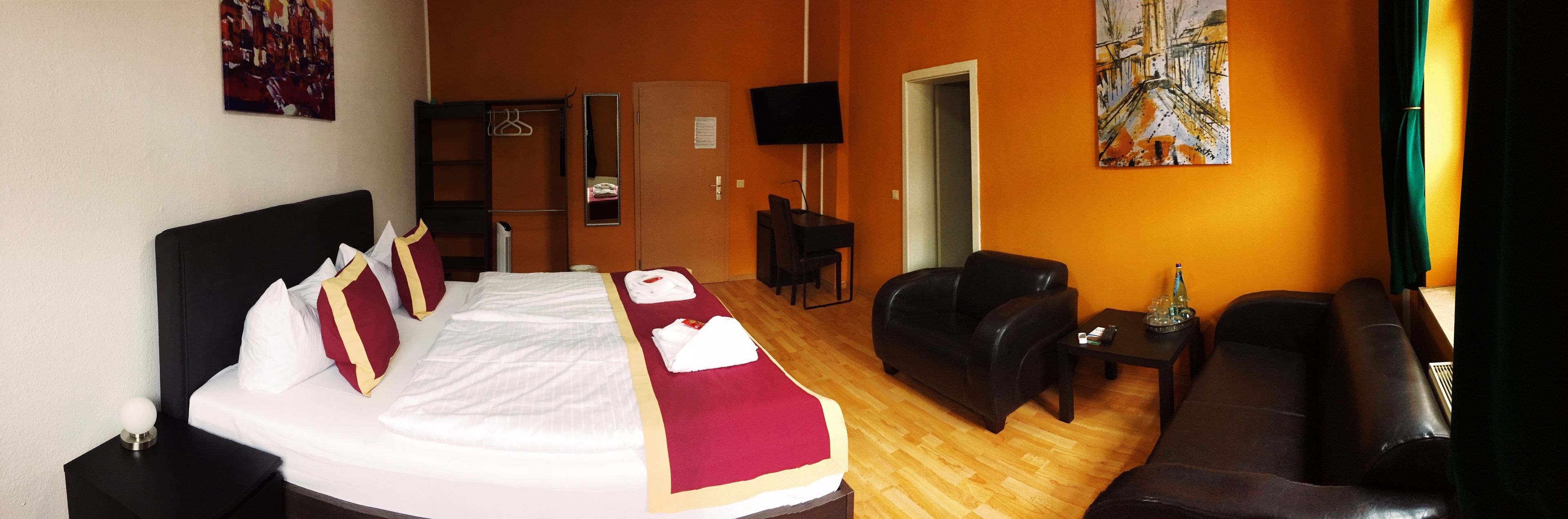 A hotel room with a bed, a sofa, a TV, and a painting on the wall.