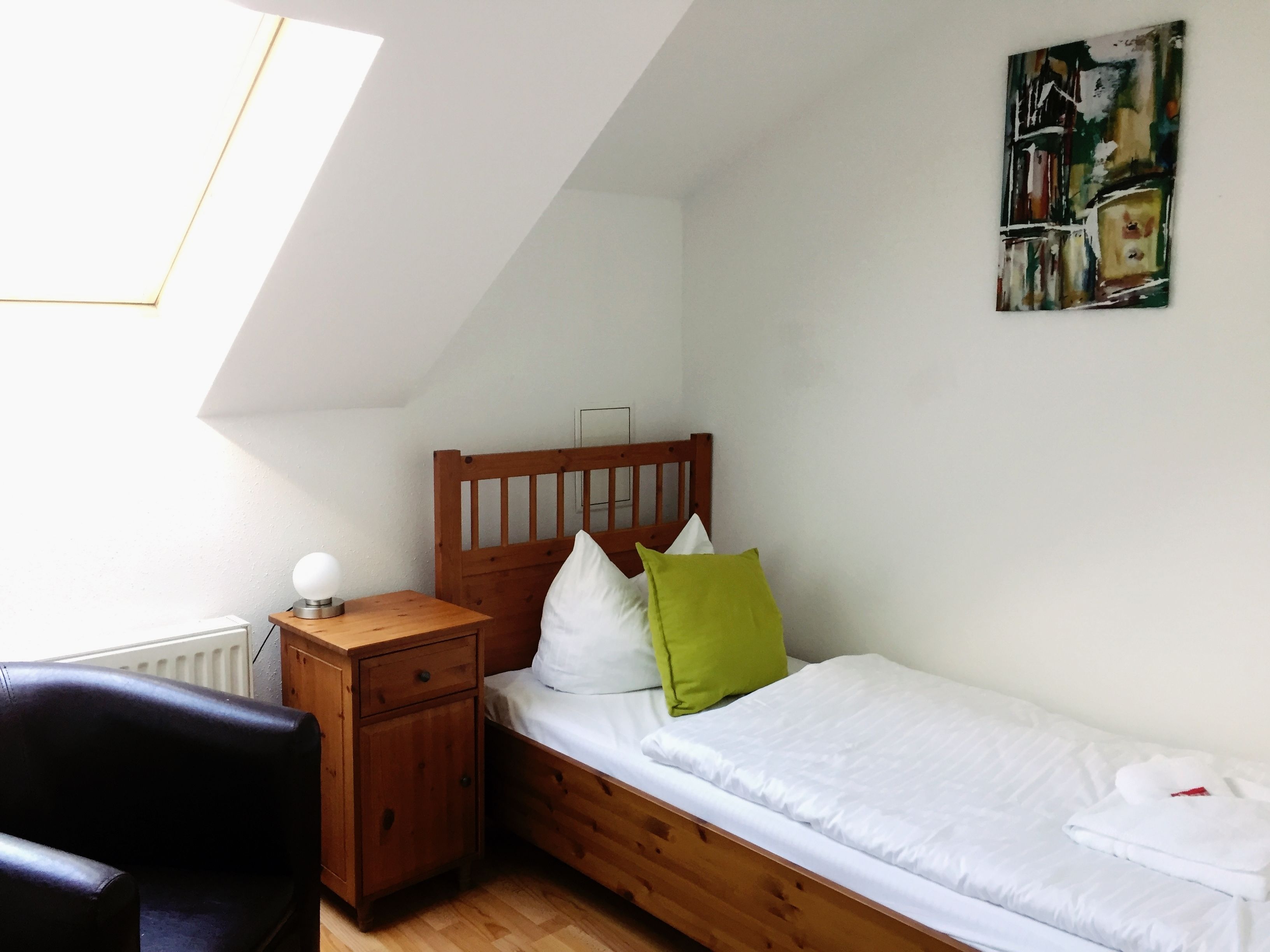 Een slaapkamer met een schuine kap, een houten bed, een nachtkastje, een stoel en een radiator.